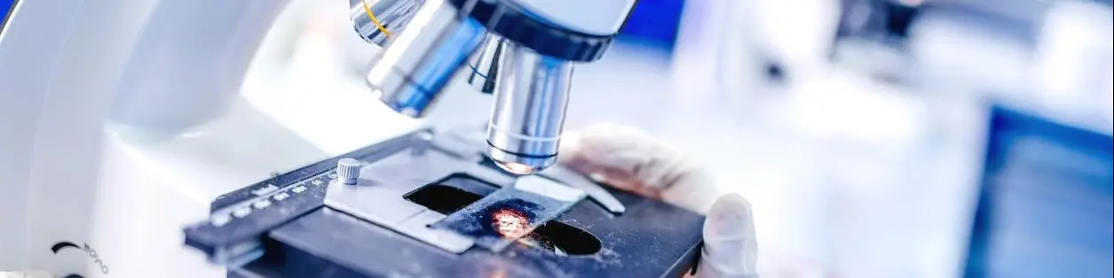 A microscope is shown with some people in the background.